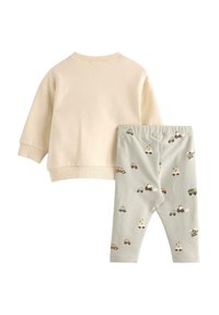 Kremowa bluza z prążkowanymi mankietami zestawiona z jasnopięknymi legginsami w kolorze zielonym, zdobionymi kolorowymi wzorami pojazdów oraz zabawnymi wzorami zwierząt.