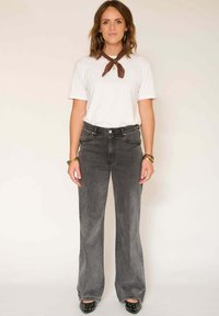 Jeans évasés gris à taille haute, associés à un t-shirt blanc et une écharpe marron. Les jeans présentent une texture délavée et un design classique à cinq poches.