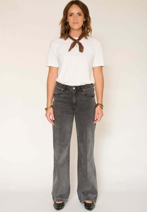 Jeans évasés gris à taille haute, associés à un t-shirt blanc et une écharpe marron. Les jeans présentent une texture délavée et un design classique à cinq poches.