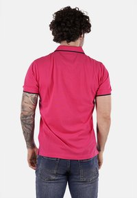 Maglietta polo in cotone rosa a maniche corte, con rifiniture blu scuro sul colletto e orlo dritto. La persona indossa jeans blu.