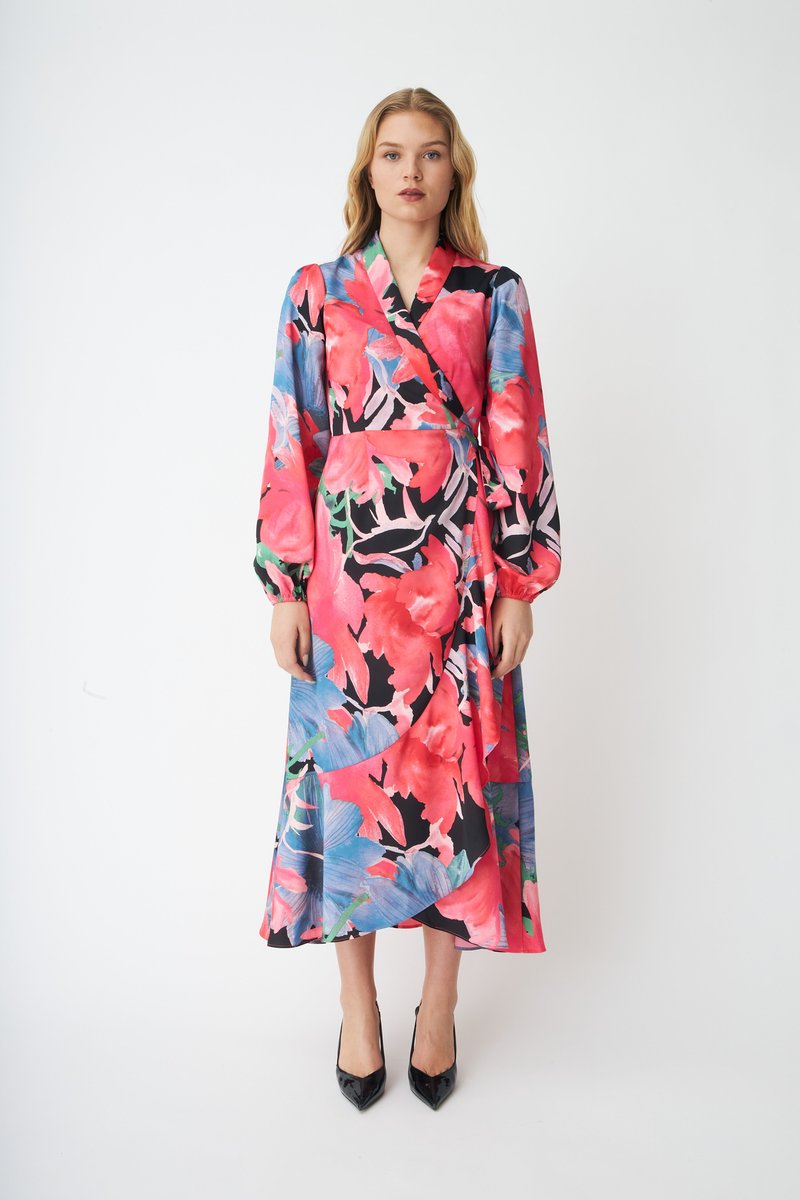 Ziedu raksta apģērbta wrap kleita rozā, sarkanā un zilā krāsā melna fona priekšā. Raksturo garās piedurknes un plūstoša silueta dizains.