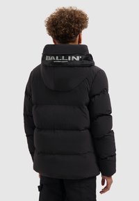 Zwarte pufferjas met capuchon, met een gewatteerd ontwerp en een glanzend "BALLIN'" logo op de achterkant van de kraag. Getextureerde stof met een gladde afwerking.