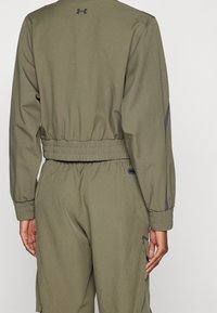 Olive green jacket with elastic waistband and cuffs. Features logo on the back and sleek design with contrasting seams.