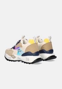 Zapatillas beige y blancas con paneles laterales iridiscentes, acentos en azul marino y amarillo, suelas blancas gruesas y texturizadas, y tiradores de tela en el talón.