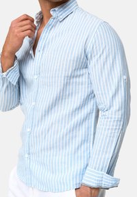 Camisa de botones a rayas azules claras y blancas, de manga larga, confeccionada en tela ligera, con cuello abotonado y detalles en los puños.