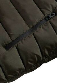 Sezione di giacca imbottita in tessuto verde scuro, con design trapuntato orizzontale e cerniera nera laterale per la chiusura.