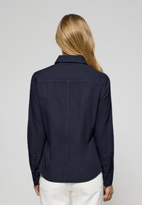 Marineblauwe overhemd met lange mouwen en een kraag, gladde textuur, knopenmanchetten en een rugnaad, gestyled voor een ontspannen pasvorm.