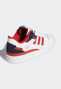 Basket blanche Adidas avec des accents rouges et noirs, une doublure rouge, trois bandes rouges sur le côté et le logo Adidas sur le talon et la semelle.