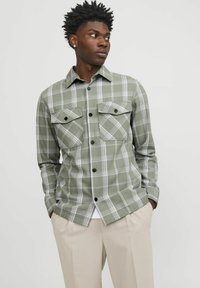 Groene geruite shirt van zachte stof, met een knoopsluiting, twee borstzakken en zwarte knopen. G gedragen over een wit shirt.