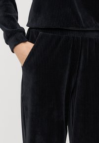 Μαύρο σετ lounge από κορδούρα με ριγωτή υφή. Διαθέτει τσέπη στο πλάι, μακριά μανίκια και χαλαρή εφαρμογή. Μαλακό και ζεστό ύφασμα.