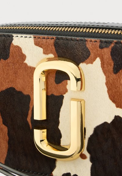 Geantă din blană artificială cu model maro și crem de piele de vacă, cu un logo lucios auriu și detalii cu fermoar negru, evidențiind suprafața texturată.