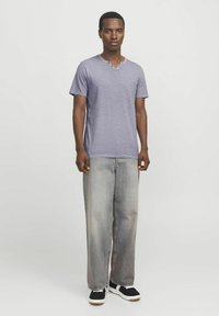 Camiseta morada de manga corta con escote en V y dos botones, combinada con jeans de pierna ancha gris claro y zapatillas negras con suelas blancas.