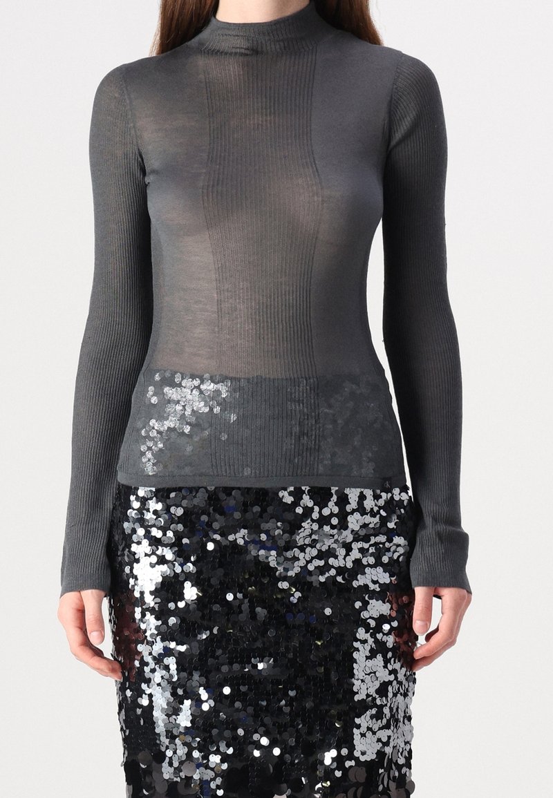 Haut gris à manches longues avec col montant, présentant une texture côtelée et une partie inférieure ornée de sequins argentés, associé à une jupe à sequins.