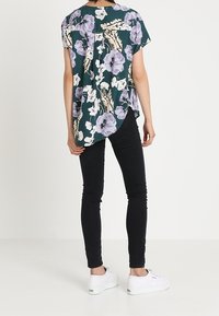 Teal pikkupaidassa on lyhyet hihat ja siihen on painettu violetin ja valkoisen kukkakuviot. Paita on yhdistetty mustiin slim fit -farkkuihin ja valkoisiin lenkkareihin, ja siinä on kaareva helma.