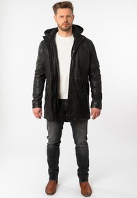 Zwarte leren jas met ritssluiting, textuurafwerking en een capuchon gevoerd met fleece, gecombineerd met grijze jeans en bruine leren laarzen.