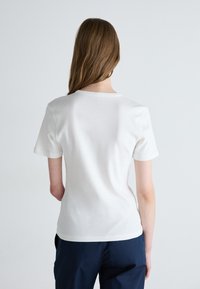 Hvit kortermet T-skjorte med rund hals, glatt tekstur og minimalistisk design. Bunnlinjen er litt buet.