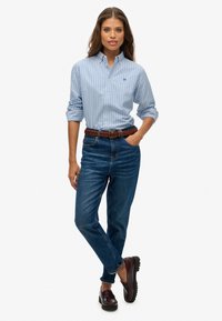 Jasnoniebieska koszula w paski na guziki, ciemnoniebieskie dżinsy, pleciony brązowy pasek oraz bordo mokasyny, podkreślające klasyczny, codzienny styl.