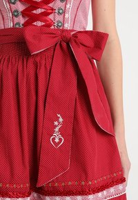 Robe rouge à motifs avec un corsage ajusté, un grand nœud à la taille, et une jupe ornée de broderies florales blanches et d'accents en dentelle.