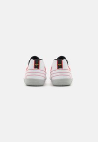 Scarpe da ginnastica bianche con accenti rossi e neri. Presentano una tomaia in rete, una suola testurizzata e dettagli di cucitura sul tallone e sui lati.