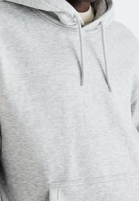 Grijze hoodie met een zachte, gestructureerde stof, koordjes en een grote voorzak. Eenvoudig ontwerp, ontspannen pasvorm.