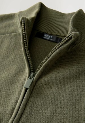 Pullover verde oliva, con texture e colletto con zip. Accenti a coste lungo il collo e i polsini. Etichetta che riporta "NEXT," made in Bangladesh.