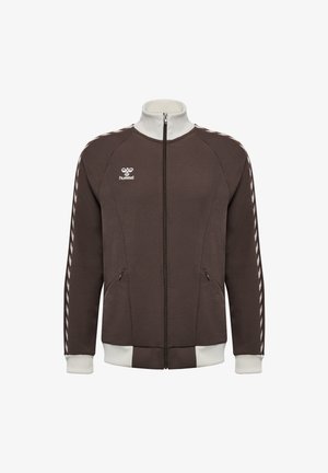 Braune Jacke mit Reißverschluss, weißem Kragen, Bündchen und Saum, mit weißen Chevron-Streifen an den Ärmeln und kleinem weißem hummel-Logo auf der Brust.