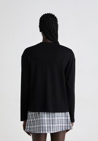Black long-sleeve top with a crew neck and relaxed fit, paired with a plaid mini skirt featuring white and gray squares.