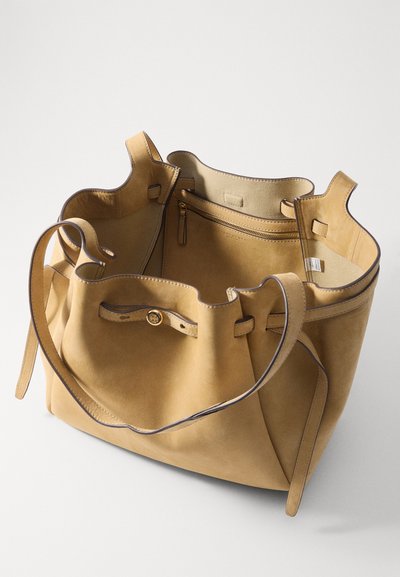 Leren emmer tas in bruin met een gladde textuur. Bevat twee banden, een handvat aan de bovenkant en een binnenzak met rits. Accentuert met contrasterende stiksels.