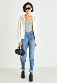 Sudadera de color crema claro, top ajustado gris, jeans azules desgastados, botines negros de tacón y un pequeño bolso negro con detalles en cadena.
