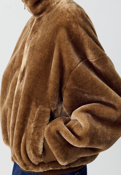 Chaqueta de pelaje sintético marrón con un alto cuello, corte oversize y bolsillos laterales. Textura suave con puños acanalados en el dobladillo.