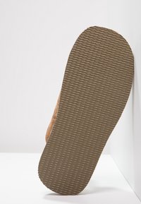 Brown suede shoe with a textured rubber sole, featuring a wavy pattern. The shoe is oriented to show the sole against a light background.