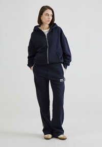 Marineblå hætte sweatshirt med frontlynlås og kængurulomme, kombineret med matchende sweatsbukser med et logotag. Teksturstof, afslappet pasform.