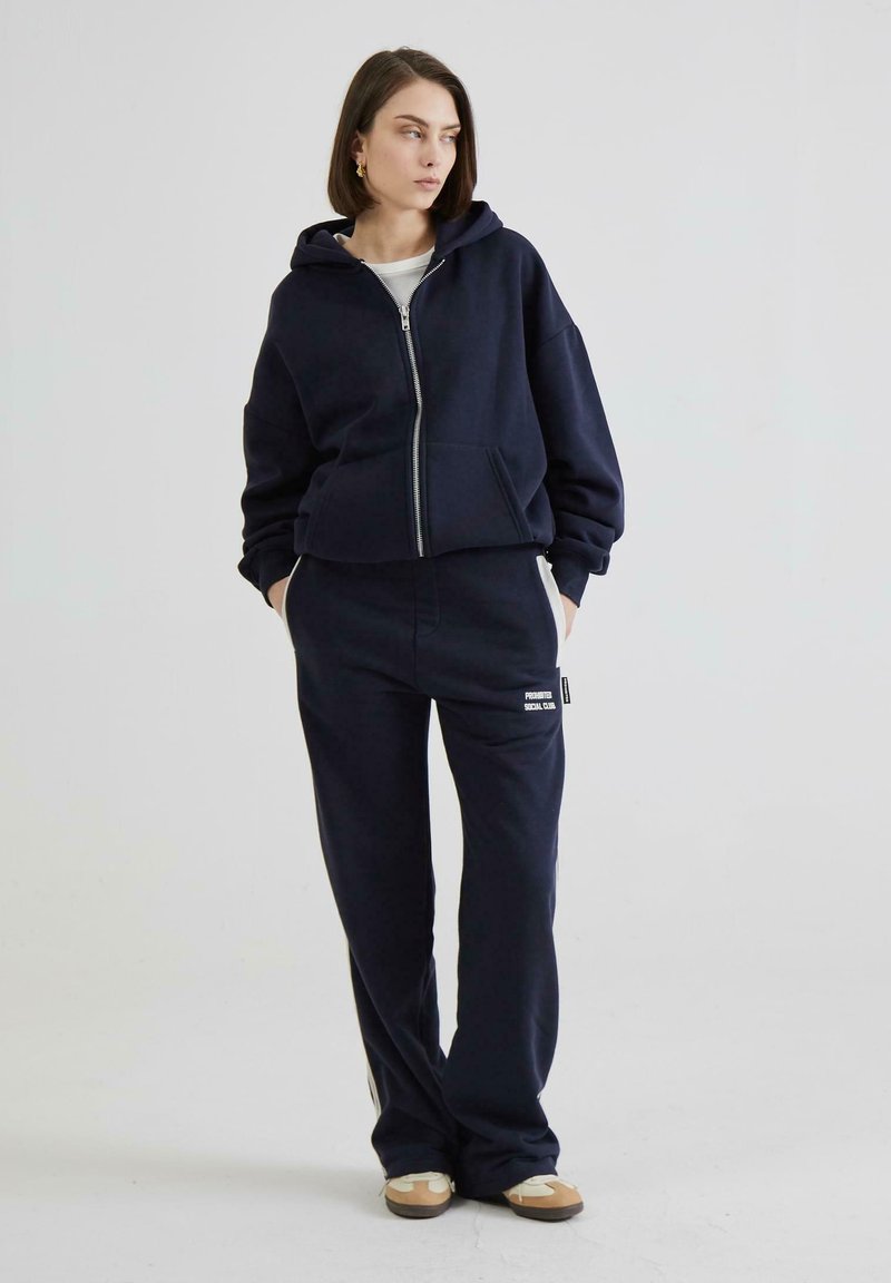 Marineblå hætte sweatshirt med frontlynlås og kængurulomme, kombineret med matchende sweatsbukser med et logotag. Teksturstof, afslappet pasform.