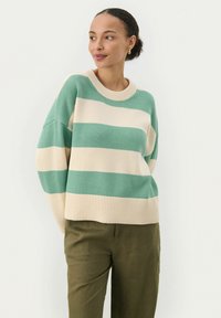 Strikket sweater med brede grønne og beige striber, ribbet rund halsudskæring og sænket skuldre. Sammen med olivengrønne bukser.