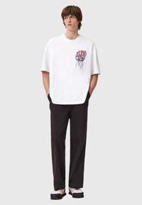 Hvit bomulls t-skjorte med korte ermer og løs passform, med et blått og rødt grafisk design på brystet. Kombinert med svarte bukser.