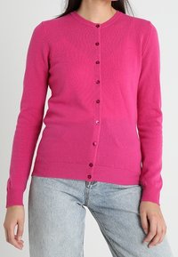 Fuchsia stickad cardigan med långa ärmar, rund halsringning och knappstängning med matchande knappar. Mjuk textur med ribbad fåll.