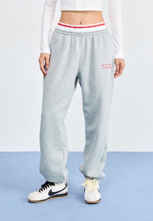 Gray sweatpants with an elastic waistband, side slits, and red printed detail. Paired with black and white sneakers. Smooth texture.
