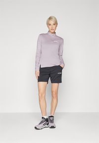 Top de manga longa roxo claro com zíper até à metade, calções pretos com logotipo e botas de caminhada cinzentas. Textura lisa, ajuste atlético.