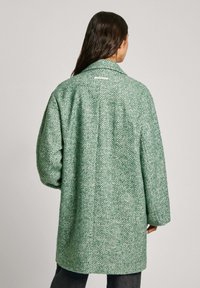 Green herringbone-pattern coat with a relaxed fit, wide collar, and soft texture, featuring a center back seam and minimalistic white tag.