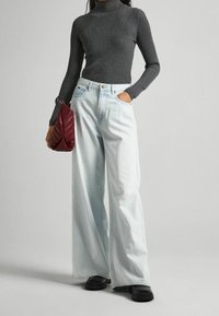 Pull col roulé gris côtelé, jean large bleu clair, et sac à main matelassé bordeaux, portés avec des chaussures plateformes noires.