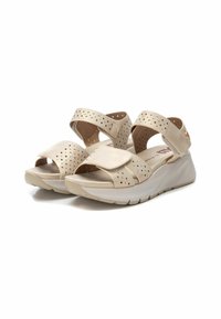 Sandalias beige con correas perforadas y una suela blanca en contraste. Cuentan con un cierre de velcro y una plantilla acolchada para mayor comodidad.