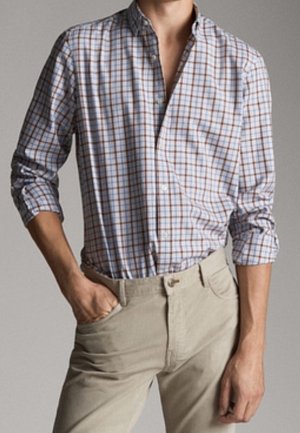 Chemise à carreaux blanche, marine et rouille, à manches longues ; associée à un pantalon ajusté de couleur claire.