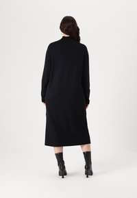 Abito lungo nero con maniche lunghe, scollatura alta e taglio dritto, abbinato a stivali neri con tacco al ginocchio. Tessuto a maglia liscio.