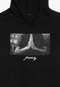 Felpa nera con cappuccio caratterizzata da una grafica frontale di mani in posizione di preghiera con tatuaggi intricati e la parola "pray" in testo bianco.