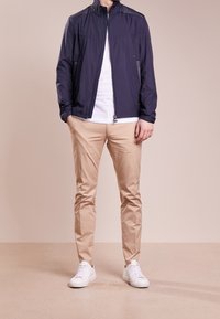 Marinblå nylonjacka med hög krage, zip-up stängning och mesh-detaljer, kombinerad med beiga chinos och vita sneakers. Slät textur genomgående.