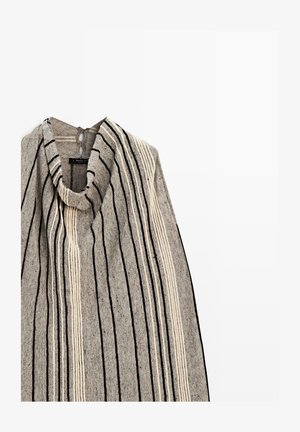 Grau gestrickter ärmelloser Poncho mit vertikalen schwarz-weißen Streifen und einem drapierten Wasserfallausschnitt, der vor weißem Hintergrund hängt.