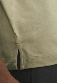 T-shirt in cotone verde oliva con taglio dritto, caratterizzato da spacco laterale all'orlo e semplici dettagli di cucitura. Tessuto morbido e design casual.