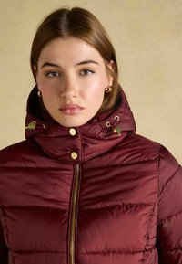 Burgundy puffer jacket with a cropped design, gold hardware, and a hood featuring drawstring details. Smooth texture with horizontal stitching.