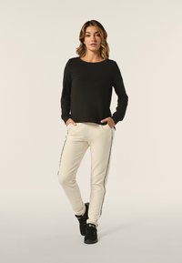 Top negro de manga larga con escote redondo. Joggers blancos con una franja lateral y bolsillos. La modelo lleva zapatillas negras.