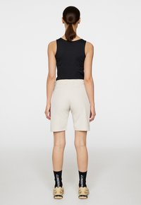 Svart ärmlös topp matchad med beigefärgade shorts i knälängd, som framhäver en mjuk textur och enkel design. Accentueras med svarta strumpor och ljusa skor.